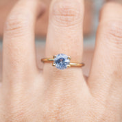 2.06ct Round Cut Ceylon Blue Sapphire ring with light blue stone set on a simple gold band, worn on finger.