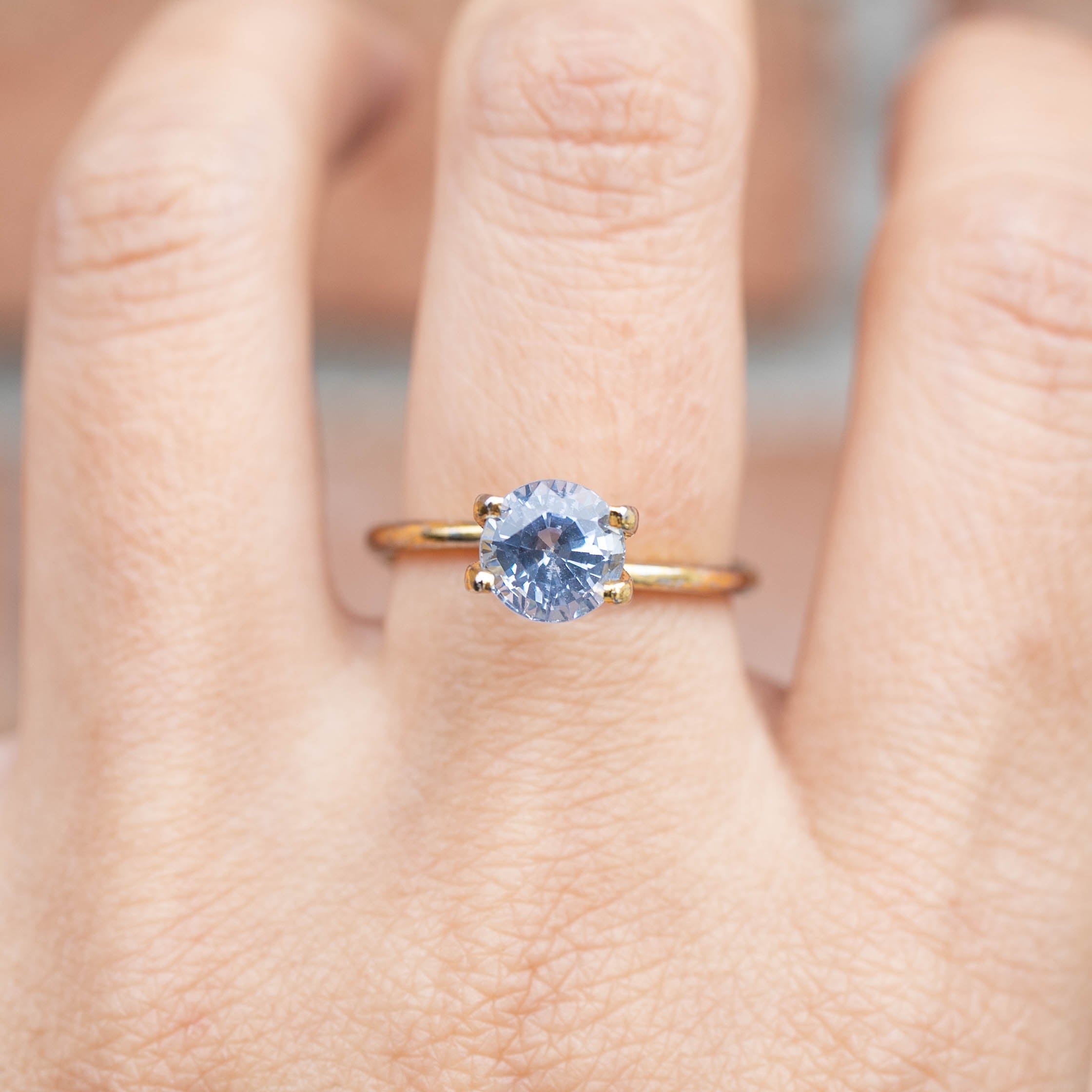 2.06ct Round Cut Ceylon Blue Sapphire ring with light blue stone set on a simple gold band, worn on finger.
