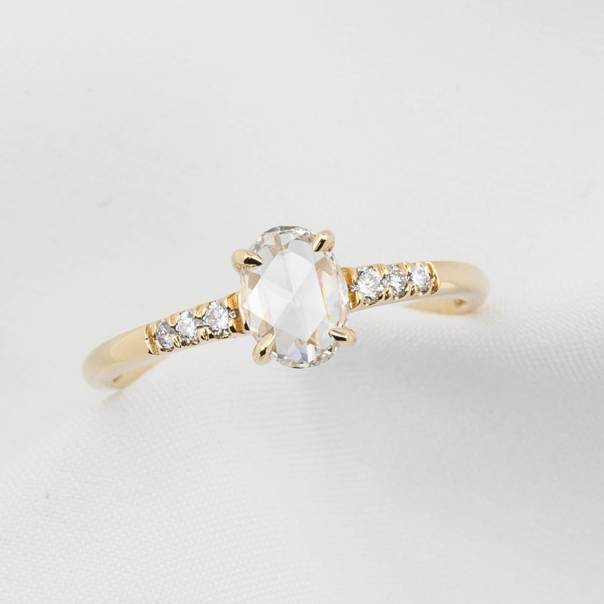 Gold ring with a central gemstone and smaller diamonds on a light gray background