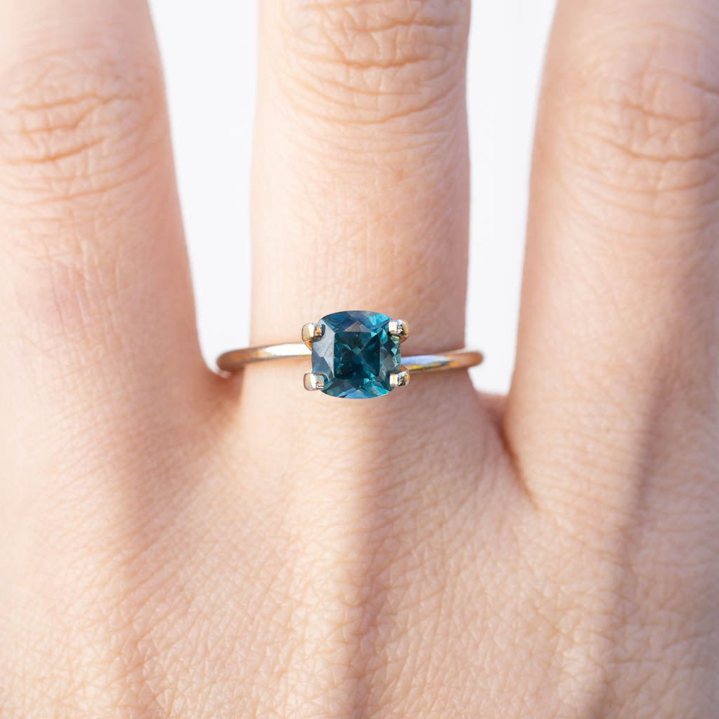 1.42ct cushion cut Montana sapphire ring in teal blue with peacock green flashes on a hand model