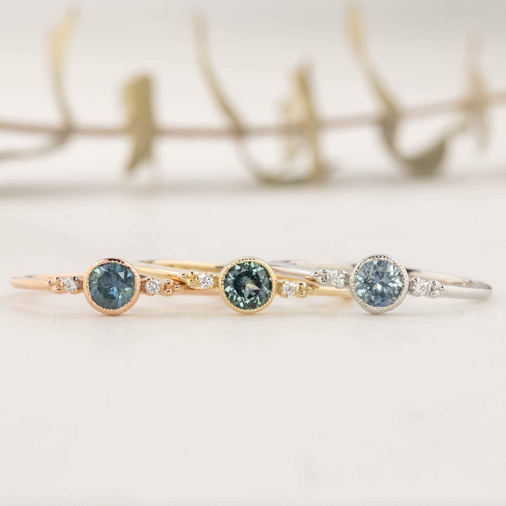 Three Estel Bezel Ring with a 0.40ct round blue-green Montana sapphire in a 14k gold setting.