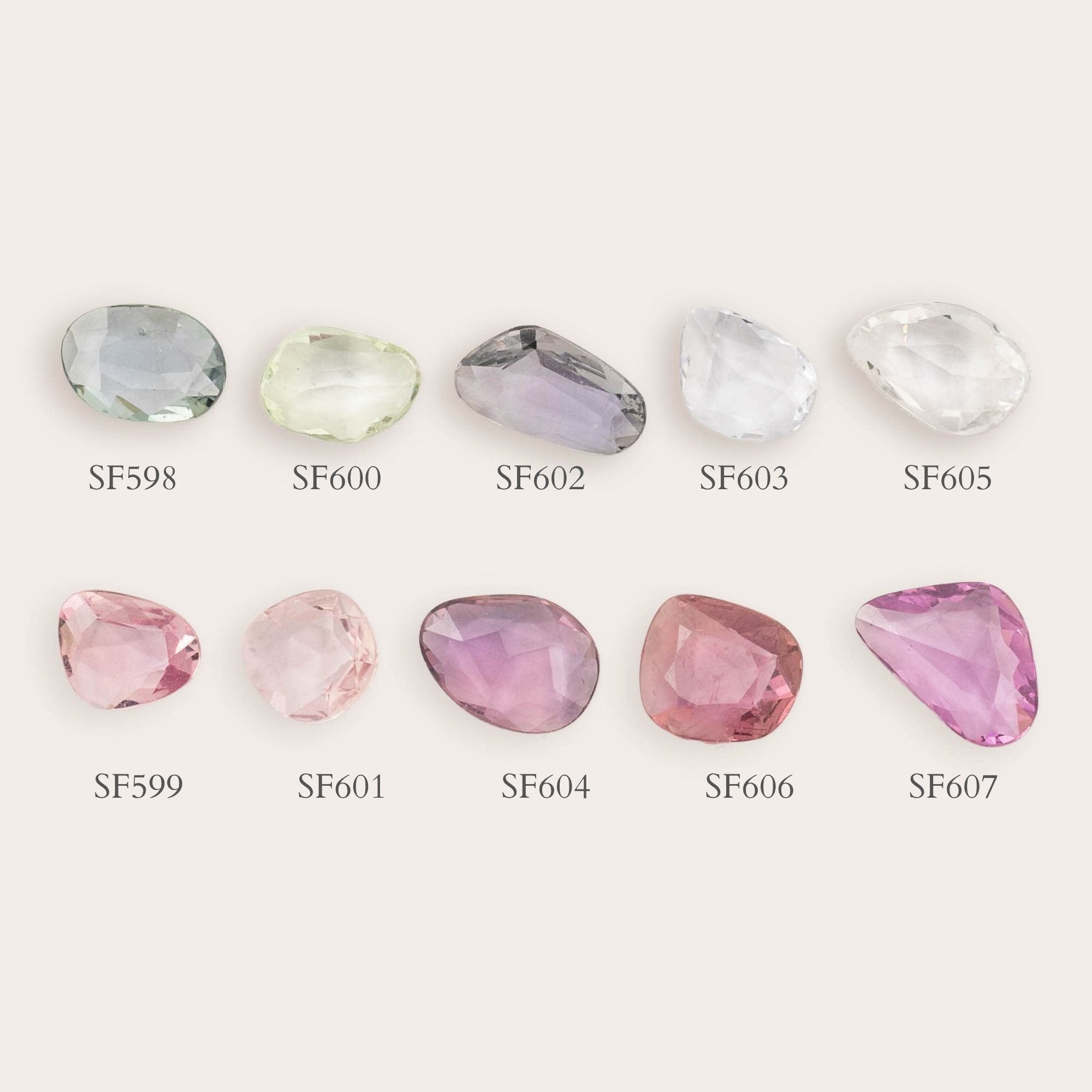 Nine loose unheated rose cut sapphires in different colors are arranged in two rows on a light warm background, each labeled with a code such as SF598, SF600, SF602, SF603, SF605, SF599, SF601, SF604, SF606, SF607.