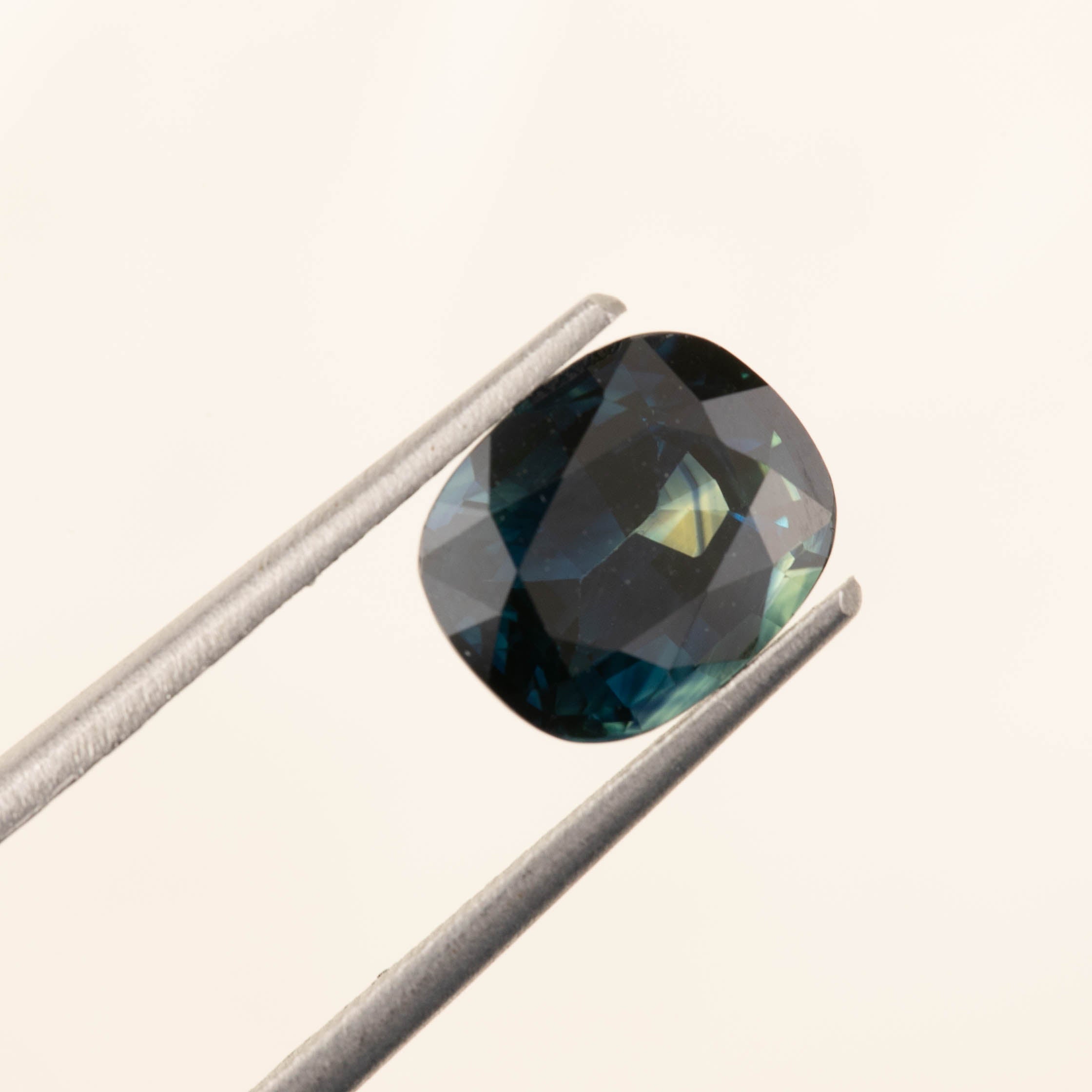 3.39ct cushion cut teal sapphire gemstone from Sri Lanka held by tweezers against a neutral background