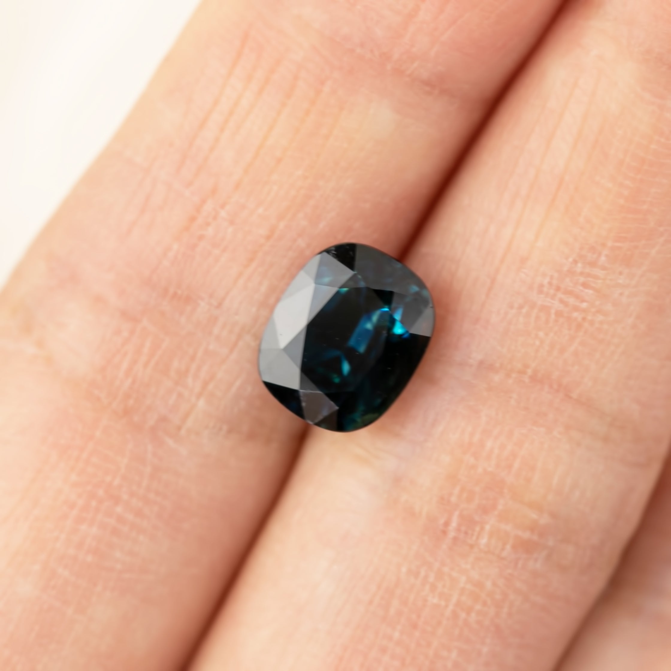 3.39ct cushion cut teal blue sapphire from Sri Lanka with VVS clarity and heat treatment shown on finger